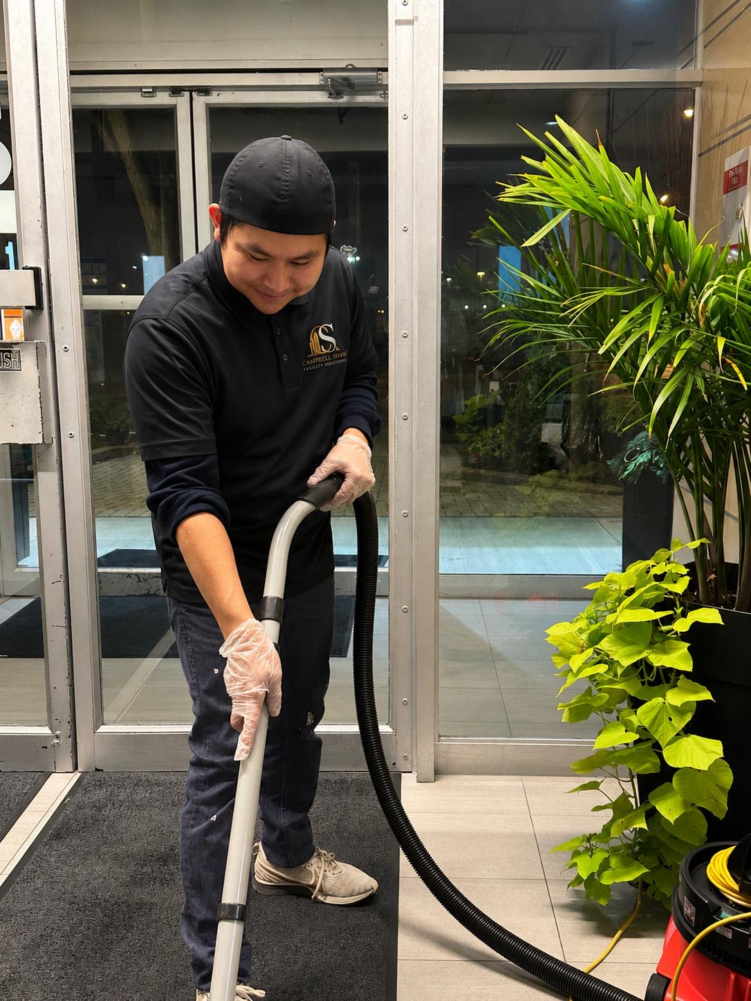 Campbell Shaw team member vacuuming an entrance mat in a commercial lobby at night