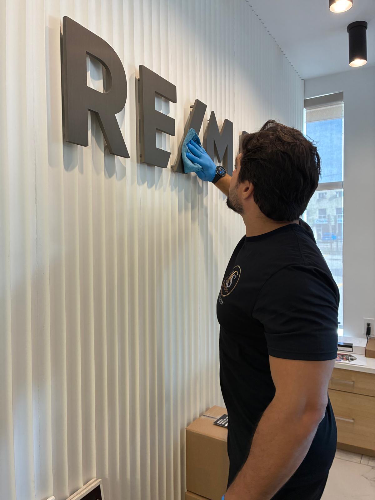 Campbell Shaw team member in a branded shirt cleaning dimensional metal wall lettering with a microfibre cloth