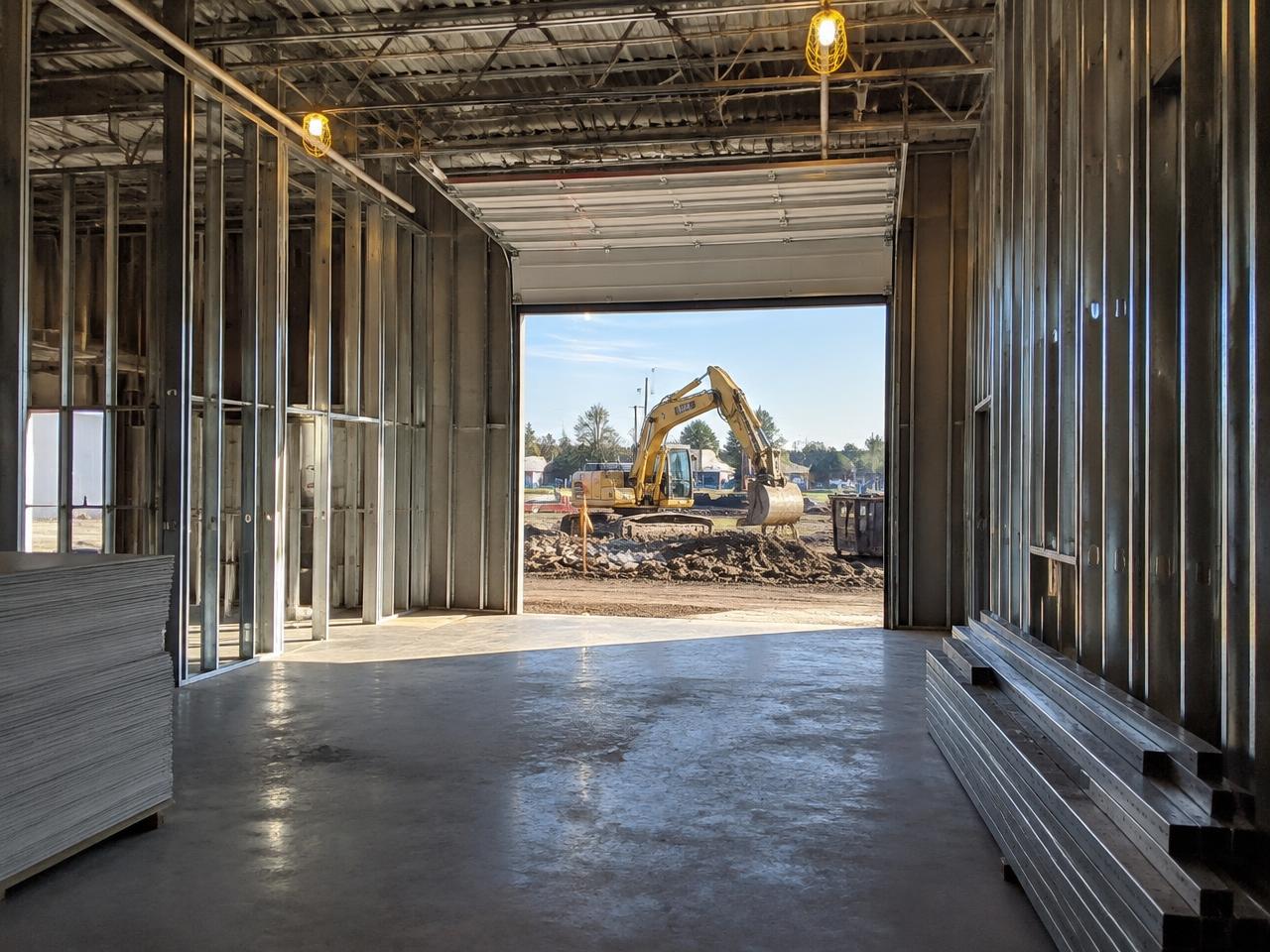 Commercial interior under renovation with steel stud framing and site excavation visible through an open bay door