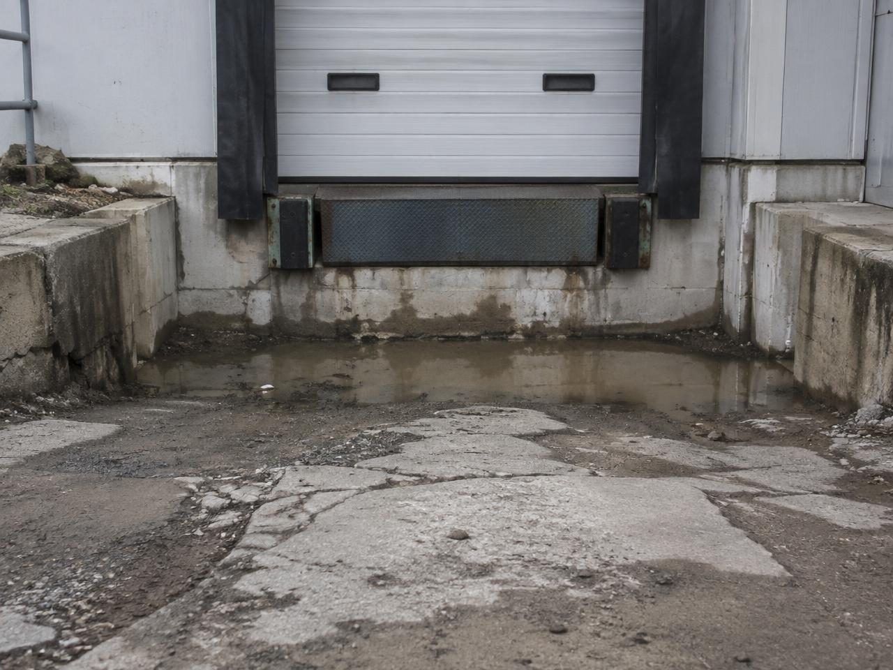 Loading dock door with a settled, cracked approach holding mud and standing water