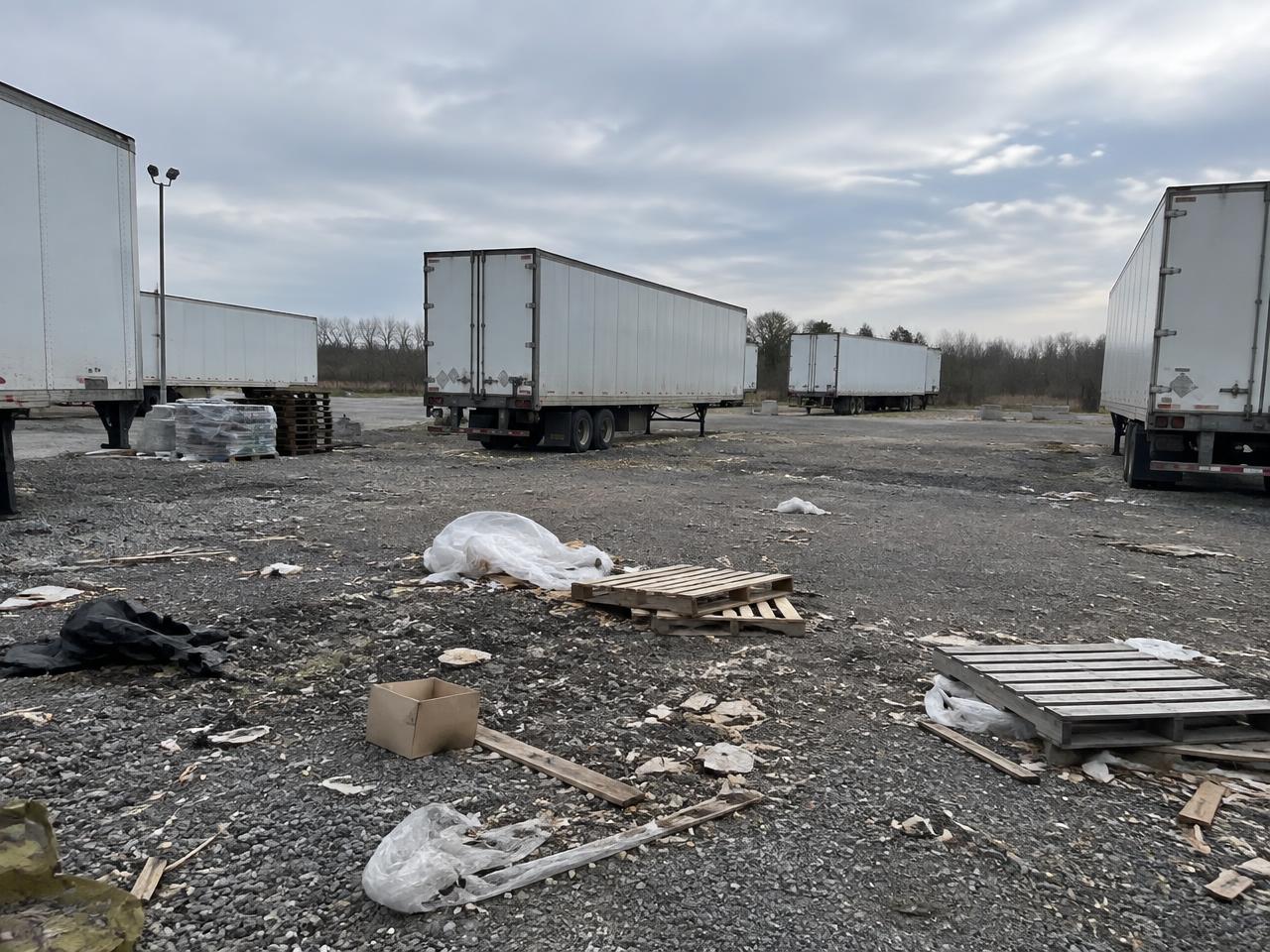 Trailer yard with pallets, plastic wrap and scattered debris across the gravel surface before clearance
